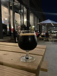 Rochester Brewing Noble Stout Beer in a glass on a picnic table outside